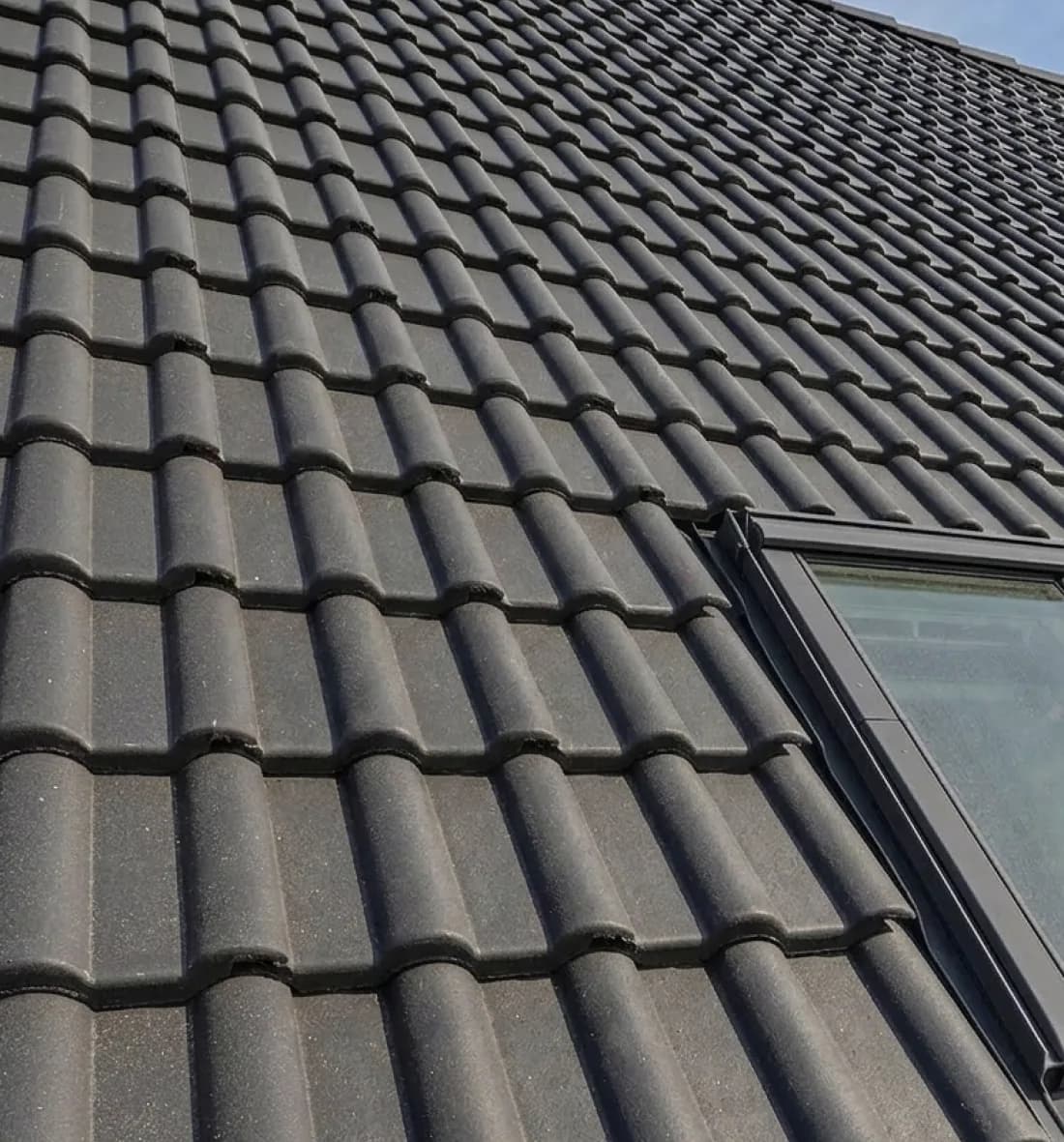 Anthrazitfarbene Betondachsteine mit Dachfenster auf einem Steildach